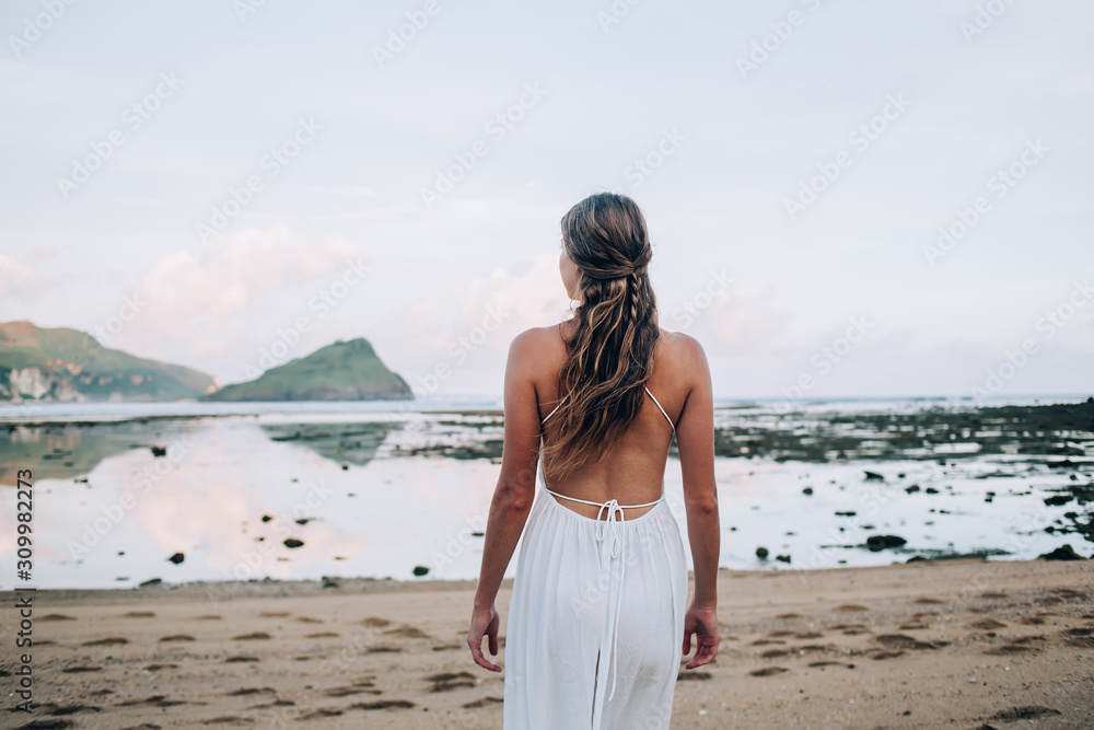 Relaxed braided woman in white dress walking along beach Relaxed braided woman in white dress walking along beach