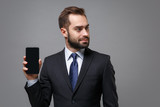 Handsome young business man in suit shirt tie posing isolated on grey background. Achievement career wealth business concept. Mock up copy space. Holding mobile phone with blank screen looking aside.