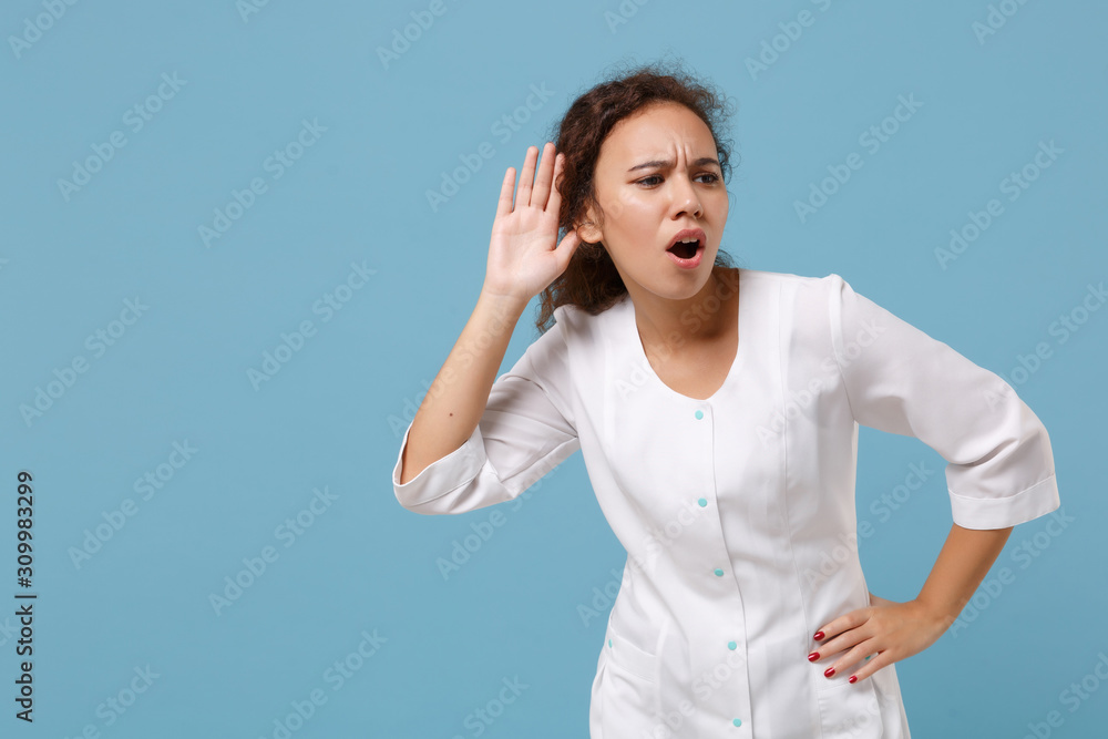 African american doctor woman isolated on blue background. Female doctor in white medical gown trying to hear you with hand near ear. Healthcare personnel health medicine concept. Mock up copy space. African american doctor woman isolated on blue background. Female doctor in white medical gown trying to hear you with hand near ear. Healthcare personnel health medicine concept. Mock up copy space.