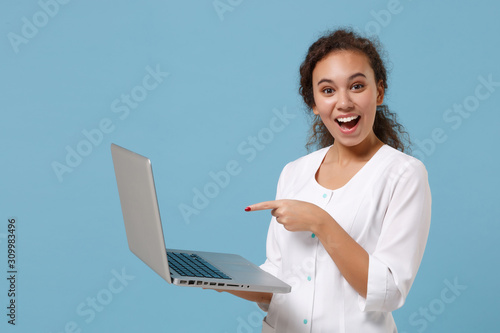 African american doctor woman isolated on blue background. Female doctor in white medical gown pointing finger on laptop pc computer. Healthcare personnel medicine health concept. Mock up copy space.