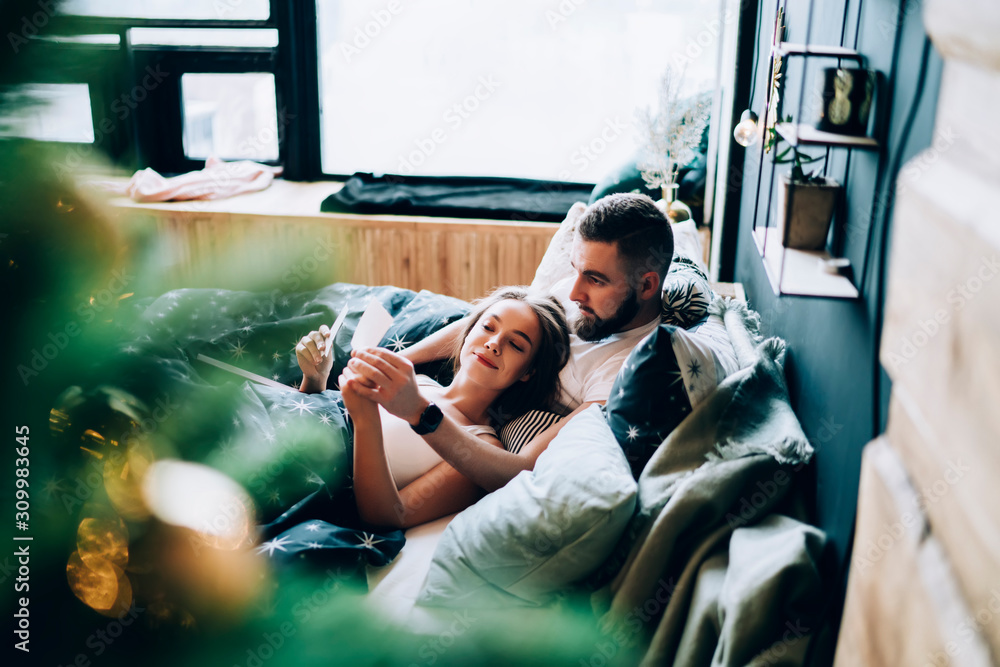Beautiful couple resting in bed with photos and reminiscing in apartment