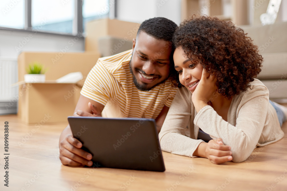 mortgage, people and real estate concept - happy african american couple with tablet pc computer lying on floor at new home mortgage, people and real estate concept - happy african american couple with tablet pc computer lying on floor at new home