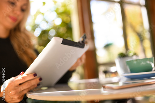 Attractive blond woman holding her tablet and credit cart by the window in a coffee shop.