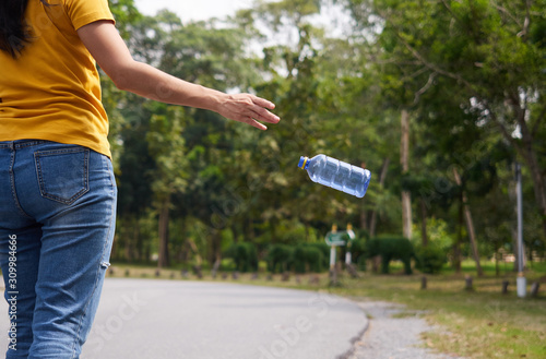 Hands of yellow shirt woman throwing empty plastic bottle in the park. Do not waste the garbage concept.
