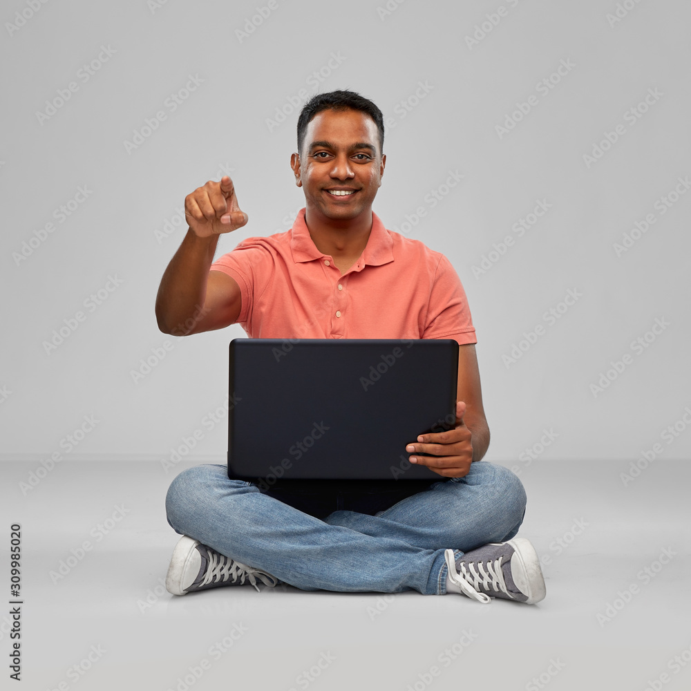 technology, internet, communication and people concept - happy indian man with laptop computer sitting on floor and pointing fnger to camera over grey background technology, internet, communication and people concept - happy indian man with laptop computer sitting on floor and pointing fnger to camera over grey background