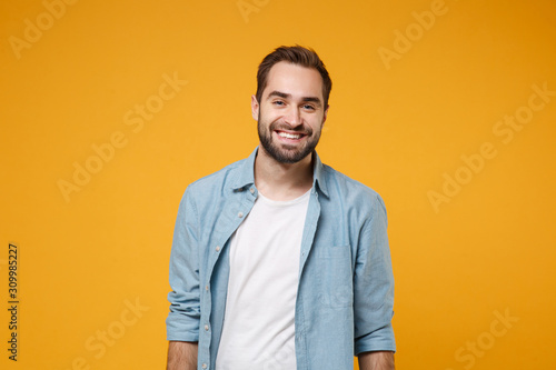 Photo Smiling handsome young bearded man in casual blue shirt posing isolated on yellow orange wall background studio portrait