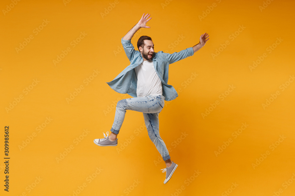 Joyful young bearded man in casual blue shirt posing isolated on yellow orange wall background studio portrait. People sincere emotions lifestyle concept. Mock up copy space. Jumping, rising hands up. Joyful young bearded man in casual blue shirt posing isolated on yellow orange wall background studio portrait. People sincere emotions lifestyle concept. Mock up copy space. Jumping, rising hands up.