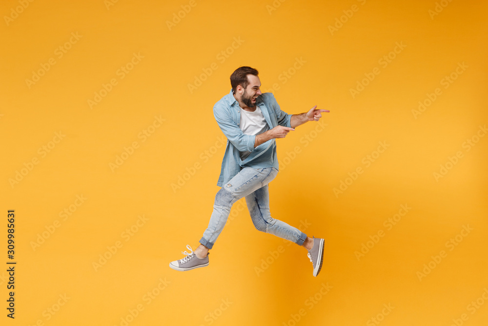 Funny young bearded man in casual blue shirt posing isolated on yellow orange background, studio portrait. People emotions lifestyle concept. Mock up copy space. Jumping pointing index fingers aside.
