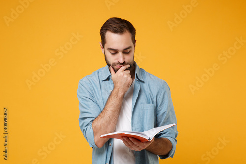 Attentive young student man in casual blue shirt posing isolated on yellow orange wall background. People lifestyle concept. Mock up copy space. Hold notebook or book reading put hand prop up on chin.