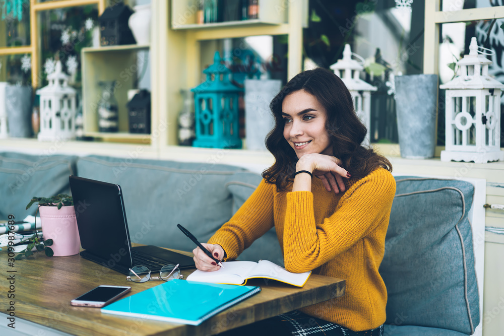 Beautiful cheerful woman writing near laptop in cafe Beautiful cheerful woman writing near laptop in cafe