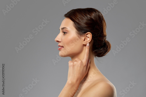 hearing, people and beauty concept - beautiful young woman pointing finger to her ear over grey background