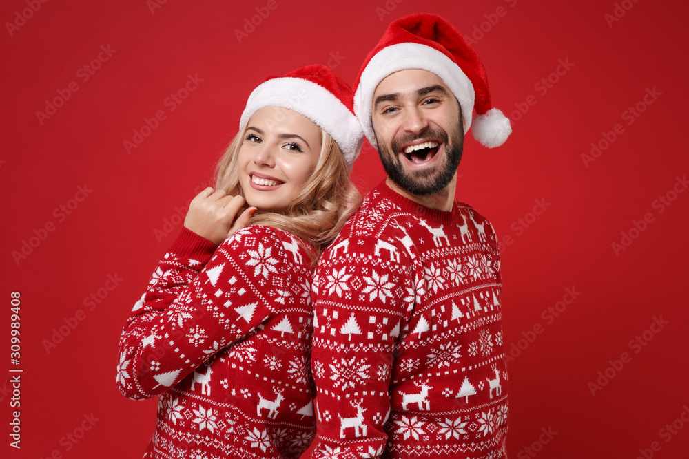 Cheerful young couple guy girl in Christmas knitted sweaters, Santa hat posing isolated on red background studio portrait. Happy New Year 2020 celebration holiday party concept. Mock up copy space. Cheerful young couple guy girl in Christmas knitted sweaters, Santa hat posing isolated on red background studio portrait. Happy New Year 2020 celebration holiday party concept. Mock up copy space.