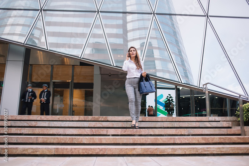Businesswoman talking on smartphone while walking down steps of modern building