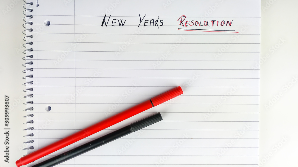 New Year resolution written on a blank sheet of paper in a notebook with pens placed on top as a motivation for improvement New Year resolution written on a blank sheet of paper in a notebook with pens placed on top as a motivation for improvement
