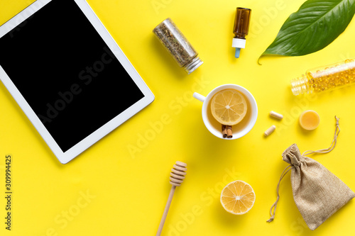 Illness concept. Composition alternative medicine. Herbal tea, ginger, lemon and gadget on a yellow background. Flat lay. View from above. Copy space