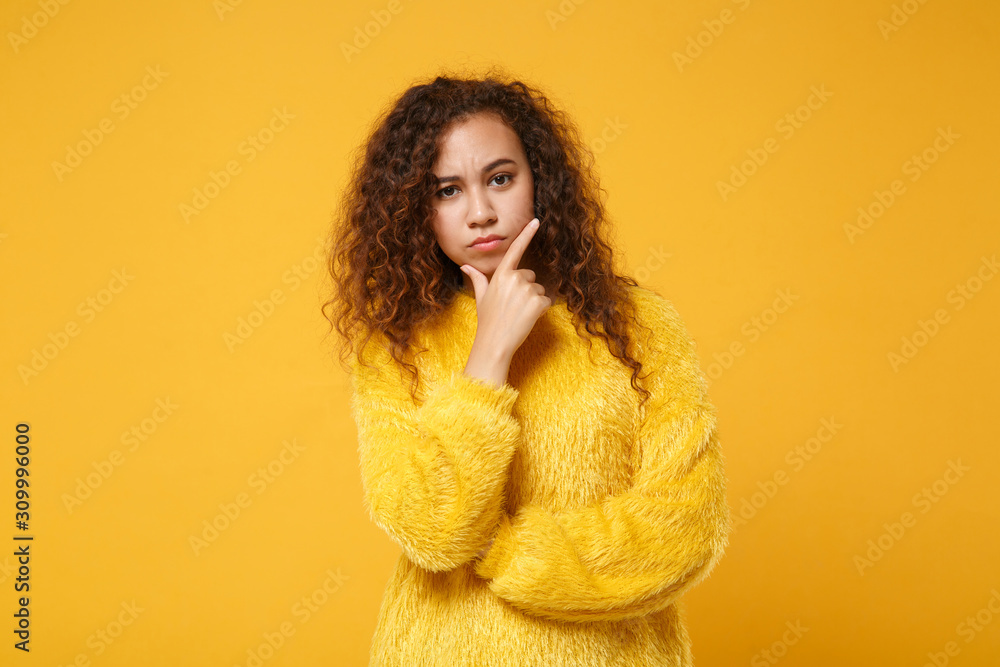 Pensive young african american girl in fur sweater posing isolated on yellow orange background studio portrait. People sincere emotions lifestyle concept. Mock up copy space. Put hand prop up on chin. Pensive young african american girl in fur sweater posing isolated on yellow orange background studio portrait. People sincere emotions lifestyle concept. Mock up copy space. Put hand prop up on chin.