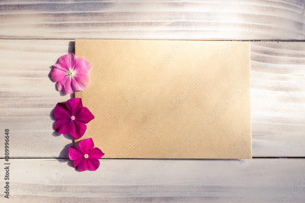 Piece of paper, envelope, with three pink flowers on wooden background. Piece of paper, envelope, with three pink flowers on wooden background.