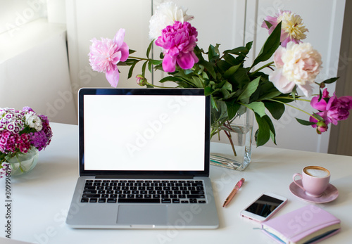 Female office desk workspace homeoffice mock up with laptop, pink peony flowers bouquet, smartphone, pink accessories and pink cup of coffee. Fashion, beauty or lifestyle blog concept.