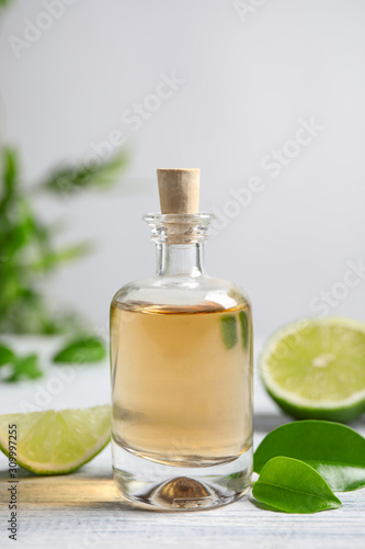 Lime essential oil and cut citrus fruits on white wooden table