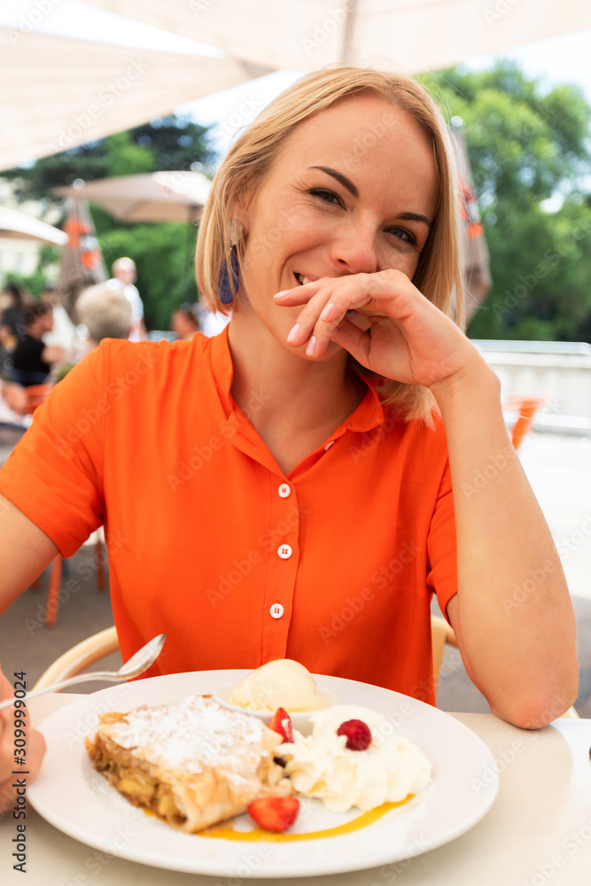 Young woman sits in a cafe in Vienna and eats Austria's traditional sweet apple strudel with whipped cream and vanilla ice cream, Vienna, Austria Young woman sits in a cafe in Vienna and eats Austria's traditional sweet apple strudel with whipped cream and vanilla ice cream, Vienna, Austria