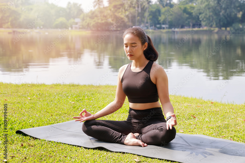 Asian woman practicing yoga in lotus position in outdoor park.