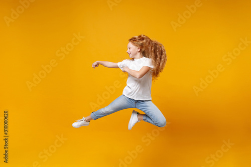 Side view of little ginger kid girl 12-13 years old in white t-shirt isolated on yellow background children portrait. Childhood lifestyle concept. Mock up copy space. Having fun, fooling around, jump.