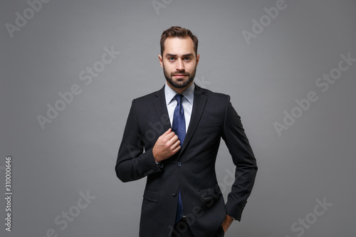 Handsome young bearded business man in classic black suit shirt tie posing isolated on grey background studio portrait. Achievement career wealth business concept. Mock up copy space. Looking camera.