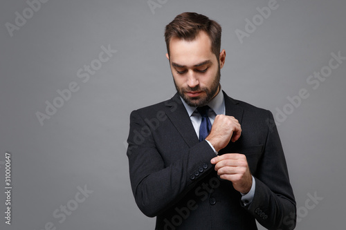 Handsome young business man in classic black suit shirt tie posing isolated on grey background studio portrait. Achievement career wealth business concept. Mock up copy space. Straightening sleeves.