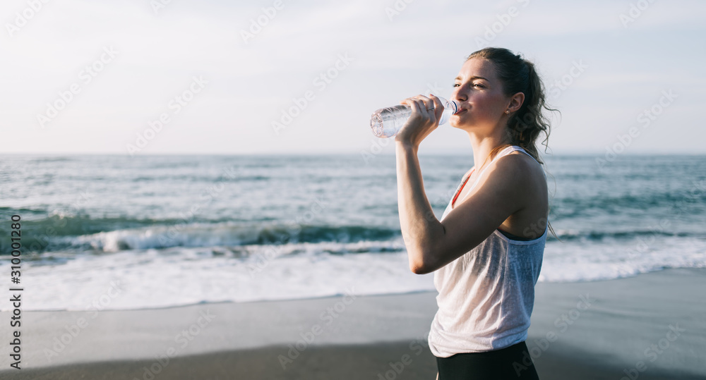 Young woman drinking water from bottle on beach Young woman drinking water from bottle on beach