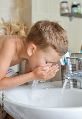 baby boy washing his face in bathroom over sink