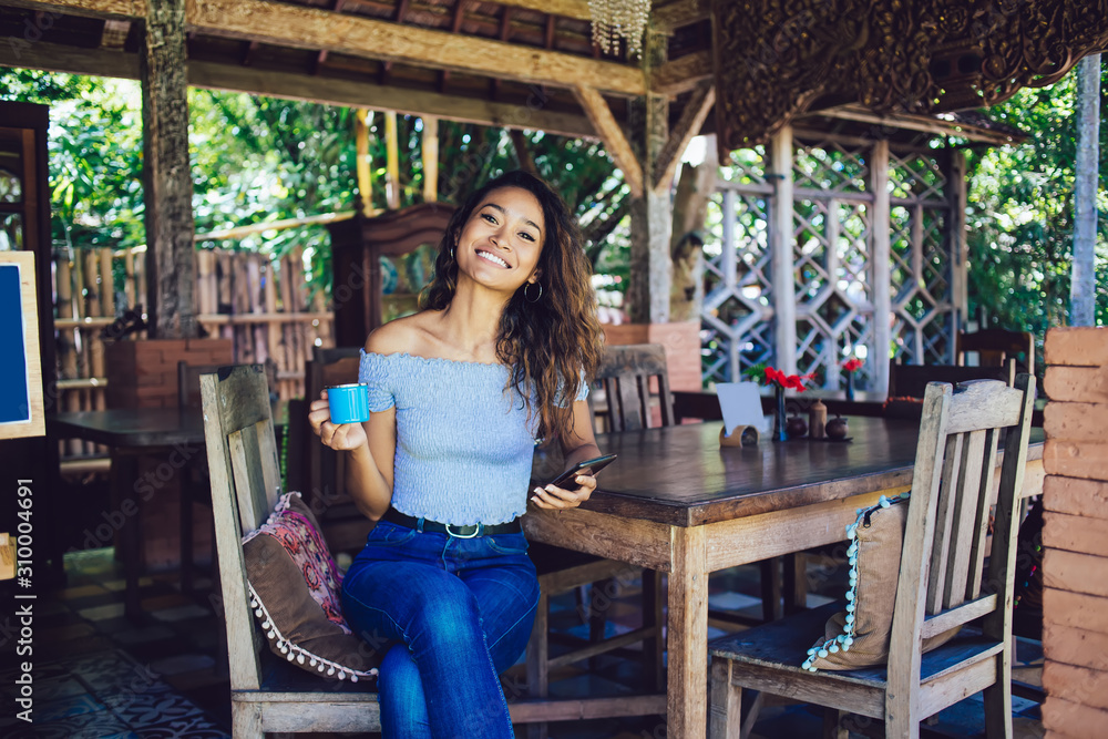 Beautiful curly woman holding phone and cup in hand