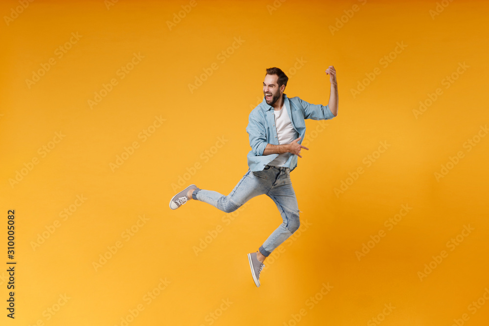 Funny young bearded man in casual blue shirt posing isolated on yellow orange wall background studio portrait. People lifestyle concept. Mock up copy space. Jumping fooling around like playing guitar.