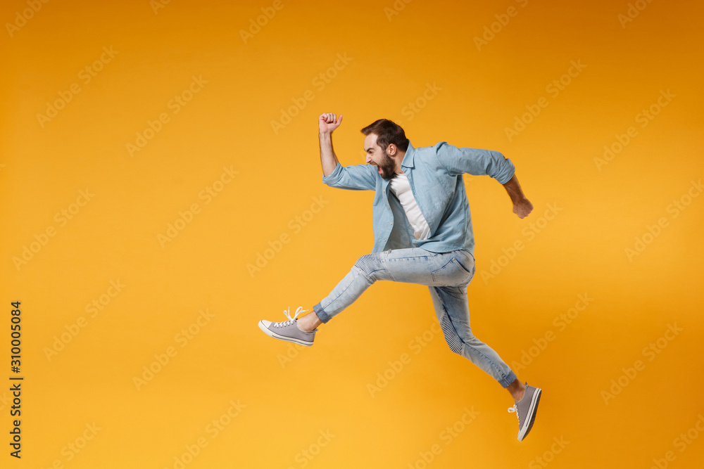 Side view of crazy young bearded man in casual blue shirt posing isolated on yellow orange background studio portrait. People sincere emotions lifestyle concept. Mock up copy space. Jumping, running.
