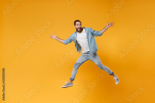 Excited young bearded man in casual blue shirt posing isolated on yellow orange wall background studio portrait. People emotions lifestyle concept. Mock up copy space. Jumping, spreading hands, legs.