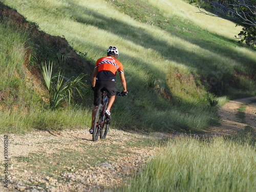 male athlete mountainbiker rides a bicycle along a countryside trail. Morning sunny. Back view.