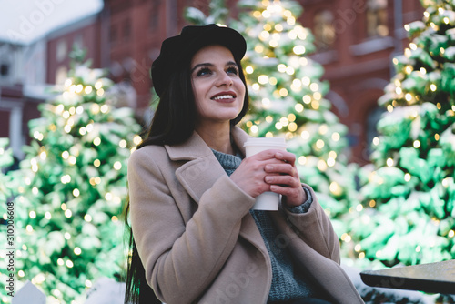 Young beautiful woman in coat with coffee cup on street with Christmas trees