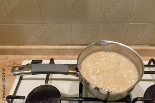 Oatmeal porridge cook in a metal silver saucepan on a gas stove.