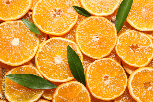 Slices of fresh ripe tangerines and leaves as background, top view. Citrus fruit
