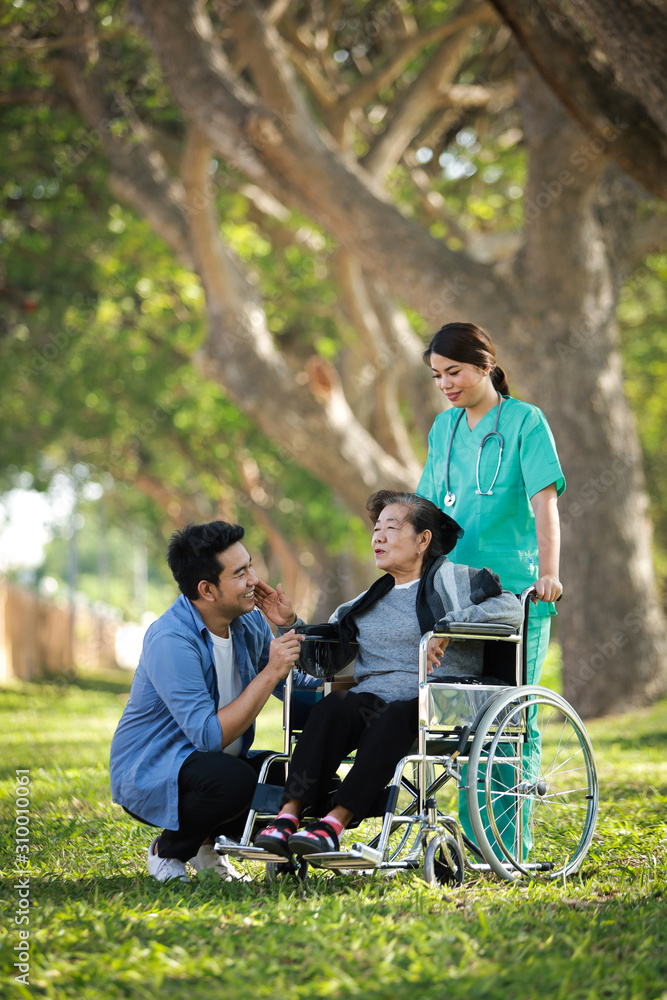 Asian senior woman sitting on the wheelchair with her son happy smile face on the green park Asian senior woman sitting on the wheelchair with her son happy smile face on the green park
