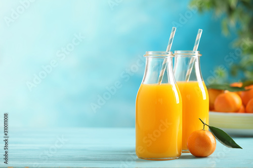 Bottles of fresh tangerine juice on blue wooden background. Space for text