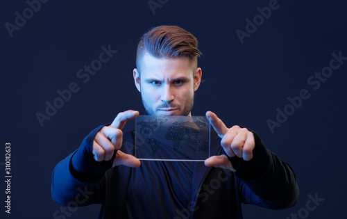 Young man with beard and trendy hairstyle uses futuristic smartphone with transparent display. Future technology, innovative ideas concept. Blue neon light. Free space for text. Dark background.