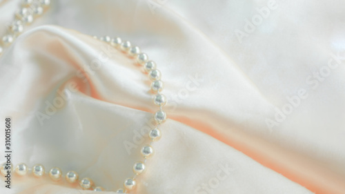 Defocused luxury silk background with a string of pearls. Delicate pastel shade. Pastel colors, concept of comfort and sexuality.