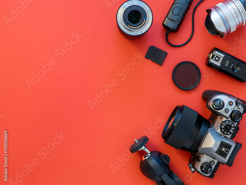 Photographer workplace with dslr camera, lens, pen tablet and camera accessories on red background. Camera, photography, visual content concept. Flat lay or top view. Copy space for text or design