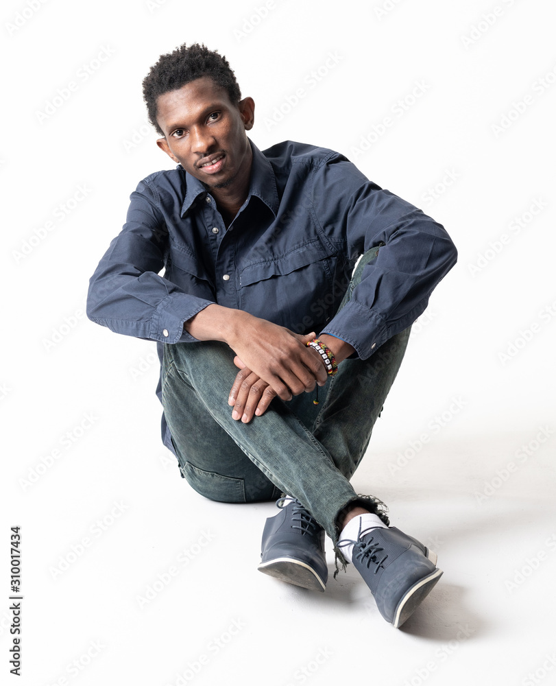 A black guy (man) in a blue shirt and jeans is sitting on a white background A black guy (man) in a blue shirt and jeans is sitting on a white background