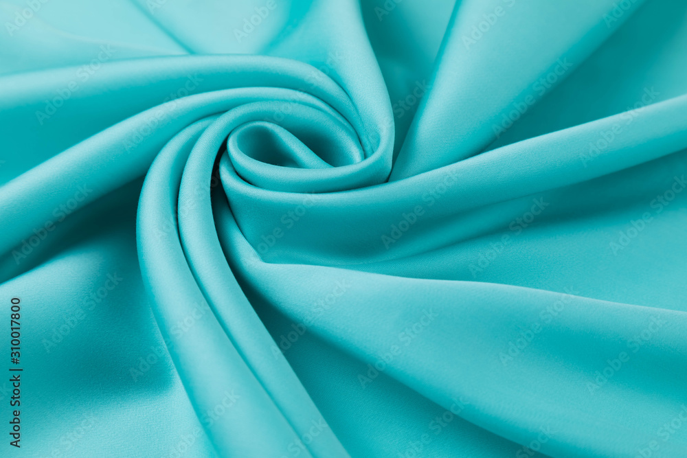 The blue satin fabric is laid out on the table in a spiral view. Soft folds of a drapery, Silky surface The blue satin fabric is laid out on the table in a spiral view. Soft folds of a drapery, Silky surface