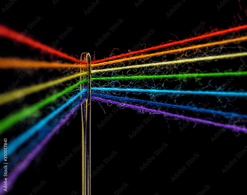 Multicolored threads, forming the colors of the rainbow, are threaded ...
