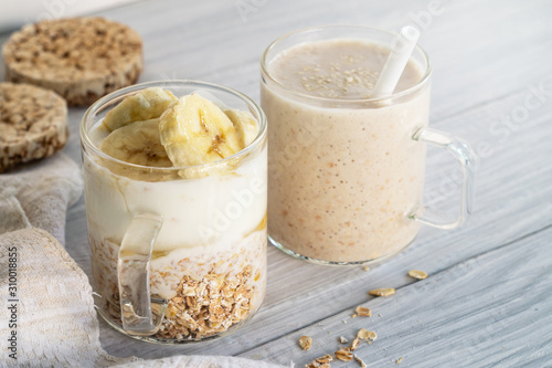 Two glass cups with ingredients banana, oatmeal and yogurt and cooked smoothie