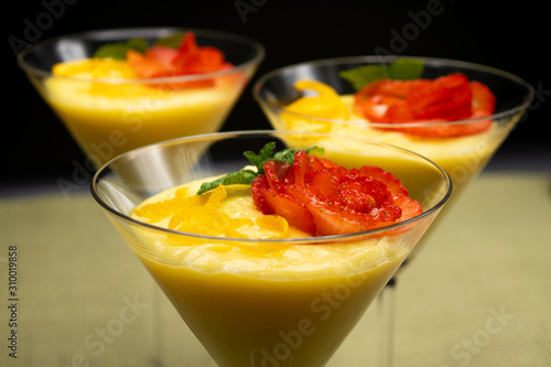 Vanilla Pudding with lemon and strawberry garnish in Martini glass with black background.