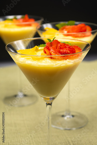 Vanilla Pudding with lemon and strawberry garnish in Martini glass with black background.