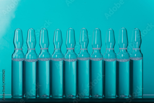 Glass medical ampoule vial for injection. Medicine is liquid sodium chloride with of aqueous solution in ampulla. Close up. Bottles ampule multicolor on background color and water. Human plasma.